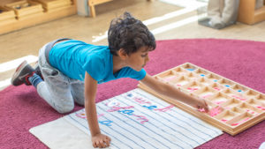 a child sits on a rug and arranges wooden letters on a mat