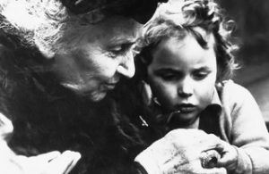 Dr. Maria Montessori leans closely next to a young girl