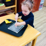 A young girl in a blue shirt holds a knife and slices a banana