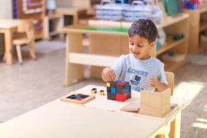 A young boy with dark hair and a grey t-shirt works with a red and blue trinomial cube