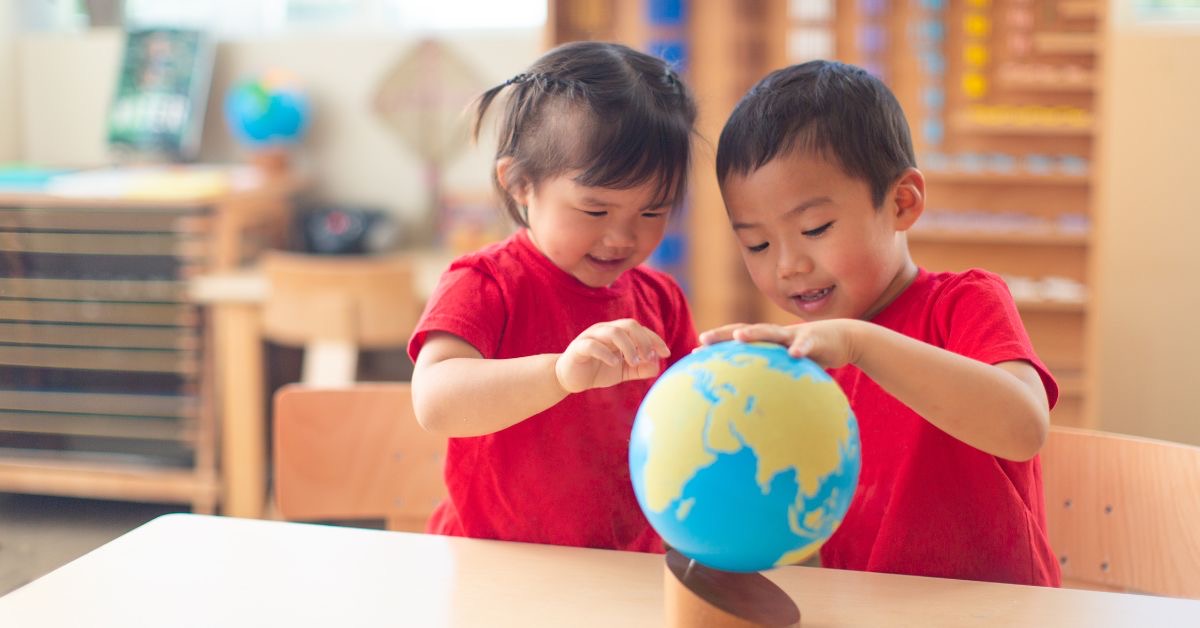 A boy and girl in red t-shirts look at a blue and green globe.