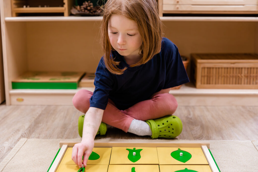 A girl with red hair and a blue t-shirt places a piece in a green and yellow puzzle