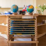 Two globes sit atop a wooden cabinet with narrow shelves housing map puzzles