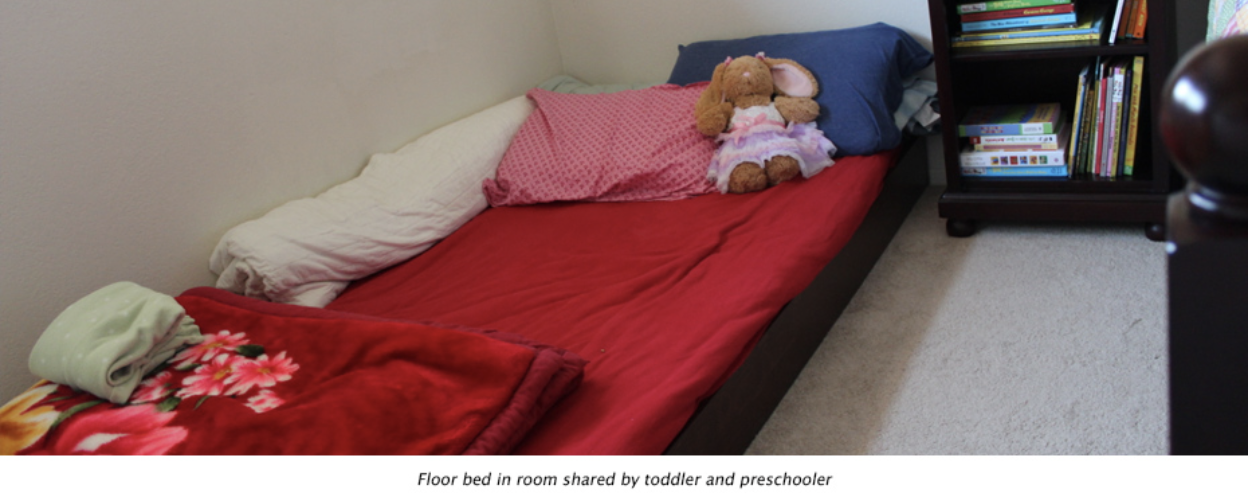 Child's bed with red blankets and a stuffed animal.