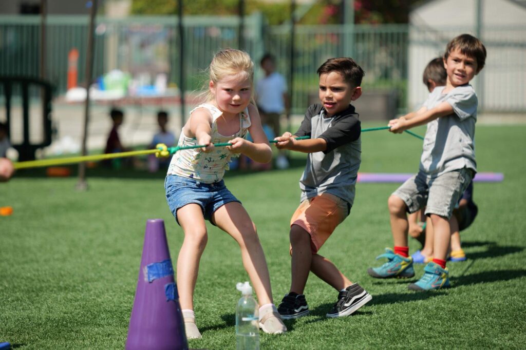 Three children play tug of war on green grass