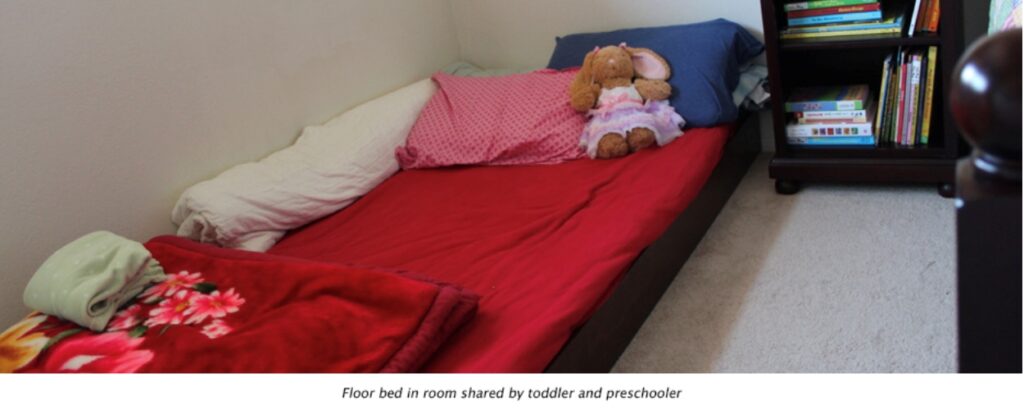 Child's bed with red blankets and a stuffed animal.